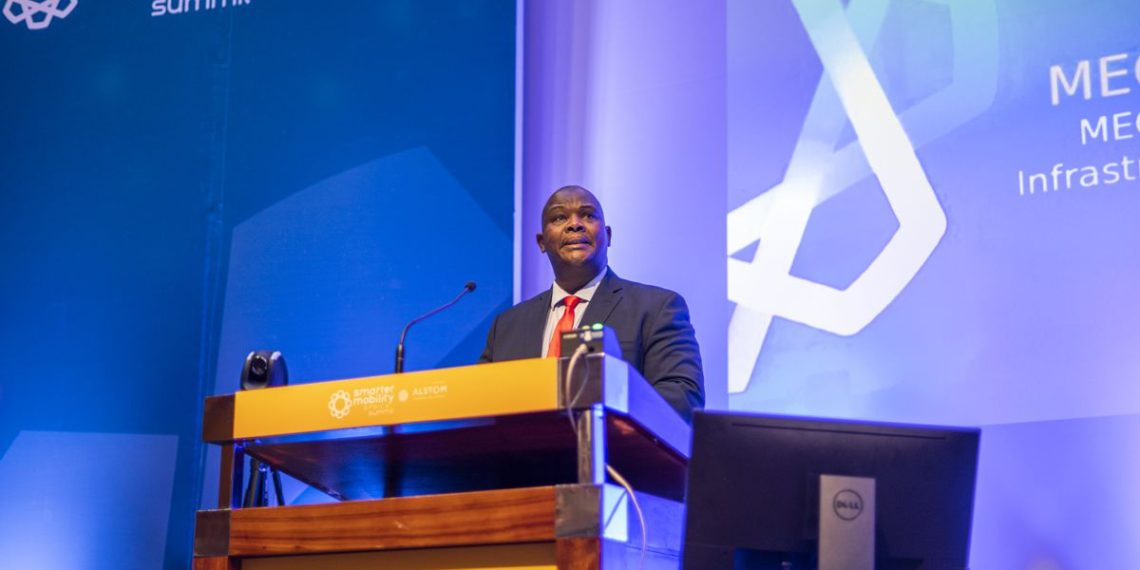 Speaker delivering a presentation at the Smarter Mobility Africa Summit with ALSTOM, standing behind a podium in a professional conference setting.