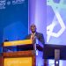 Speaker delivering a presentation at the Smarter Mobility Africa Summit with ALSTOM, standing behind a podium in a professional conference setting.